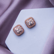 A pair of rose gold colored embellished stud earrings resting on a pale surface.